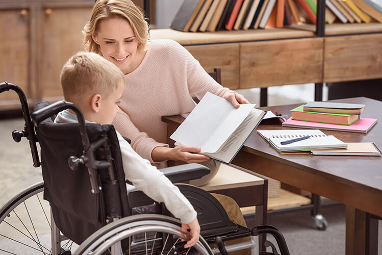 A blond woman teaching a young boy in a wheelchair.