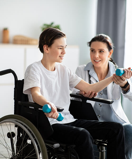 A healthcare professional helping a teenaged boy with physical therapy.